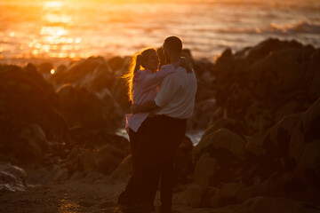 Wall Mural - A young couple in love embracing on a rocky coastline during an amazing sunset.