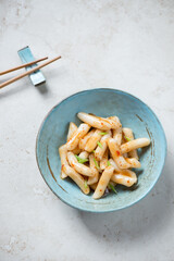 Wall Mural - Turquoise bowl with korean tteokbokki or garaetteok, vertical shot on a light-beige stone background, elevated view