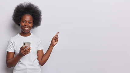 Young beautiful Afro American woman points index finger on blank space advertises product uses dressed in casual t shirt isolated over white background. Follow this direction. Click on link.