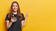 Horizontal shot of optimistic young European woman dressed in casual black t shirt holds mobile phone downloads new app points index finger above smiles toothily isolated over yellow background