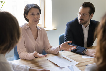 Serious mature businesswoman, company boss, executive meet with business partners talk to corporate clients at formal meeting, explain contract details, discuss cooperation, take part in negotiations