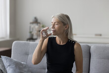 Peaceful Pretty Blonde Mature Woman Drinking Natural Mineral Water With Closed Eyes For Healthcare, Healthy Metabolism, Refreshment, Sitting On Couch At Home, Satisfying Thirst