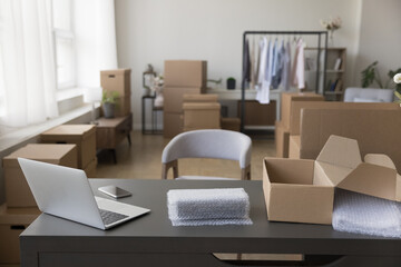 Internet store office workplace with table, computer, smartphone, paper package, wrapped product. Empty home storage place with no people, nobody, stacked cardboard boxes