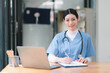 © PRIME STOCK LAB - A confident,Beautiful, professional, millennial female doctor or nurse is working online with a laptop while sitting at a desk in a hospital consultation room.