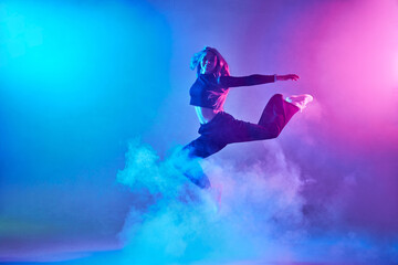 a girl in dark clothes dances on a neon background in smoke, modern dance