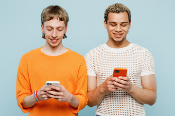 Young cool couple two gay men wearing casual clothes together hold use mobile cell phone isolated on pastel plain light blue color background studio portrait. Pride day june month love LGBTQ concept.