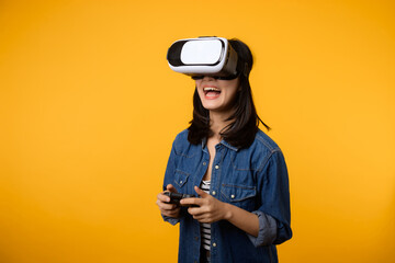 Poster - Young asian woman happy success wearing virtual reality headset game entertainment and holding joystick controller isolated on yellow background. Winner of cyber future video game concept.