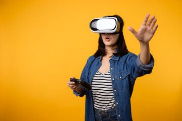 Poster - Young asian woman happy success wearing virtual reality headset game entertainment and holding joystick controller isolated on yellow background. Winner of cyber future video game concept.