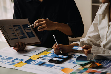Close up ux developer and ui designer brainstorming about mobile app interface wireframe design on table with customer breif and color code at modern office.Creative digital development agency