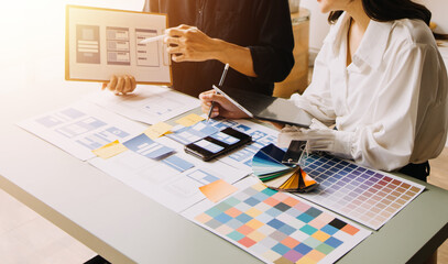 Close up ux developer and ui designer brainstorming about mobile app interface wireframe design on table with customer breif and color code at modern office.Creative digital development agency