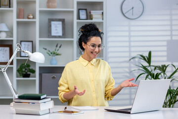 Wall Mural - Successful business woman works remotely from home, employee uses laptop for remote online communication, Hispanic woman inside home office studies online while sitting at the table.