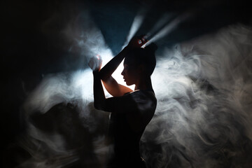 Dancer in a modern style poses against the background of smoke and flood lights.