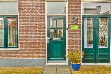 a brick building with two green doors and a blue flower pot on the sidewalk in front of the door is empty