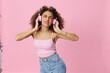 © SHOTPRIME STUDIO - Happy woman wearing headphones with curly hair listening to music and dancing in a pink T-shirt and jeans on a pink background, copy space
