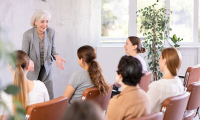 Wall Mural - Emotional aged female tutor leading educational class for group of women sitting in auditorium..