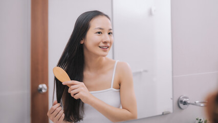 Wall Mural - Happy attractive young woman combing wet hair with comb in bathroom after shower at home. Hair care and healthy hair