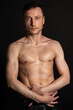 © vladorlov - Young attractive man with an athletic body on a black background.