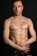 © vladorlov - Young attractive man with an athletic body on a black background.
