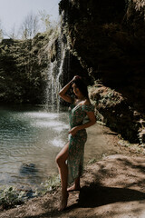 Wall Mural - Beautiful model in a turquoise dress posing near a mountain waterfall.Wildlife concept