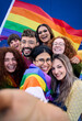 © CarlosBarquero - Vertical selfie of LGBT group of young people celebrating gay pride day holding rainbow flag together. Homosexual community smiling taking cheerful self portrait. Lesbian couple friends generation z.