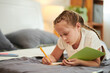 © DragonImages - Pensive preteen girl lying on bed and writing in her diary