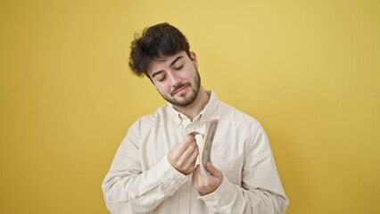 Wall Mural - Young hispanic man smiling confident counting dollars over isolated yellow background