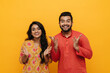 © Drobot Dean - Indian couple smiling at camera and gesturing while standing isolated over yellow background