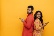 © Drobot Dean - Indian man and woman using mobile phones while standing back to back isolated over yellow background