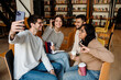 © Drobot Dean - Group of smiling students taking selfie while studying together in library