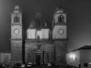 Night view in black and white of the Cathedral of Santa Margherita, Montefiascone, Italy, partially shrouded in fog