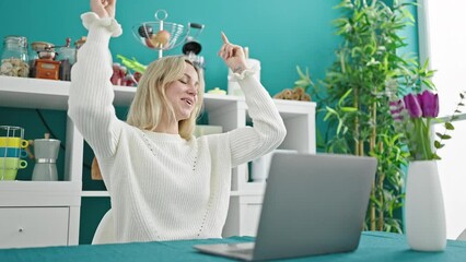 Poster - Young blonde woman using laptop dancing at dinning room