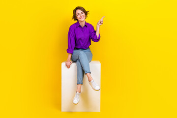 Sticker - Full body size cadre of young satisfied business promoter lady sit podium point finger novelty brand name isolated on yellow background