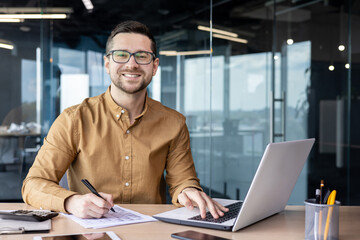 portrait of young businessman in shirt, man smiling and looking at camera at workplace inside office