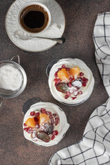 Wall Mural - Mini Pavlova cake with pomegranate, tangerines and grapes on brown background, Top view