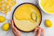 The process of cooking lemon tart. Filling the shortbread
tartlet  with lemon curd. Hands in the frame.Top view