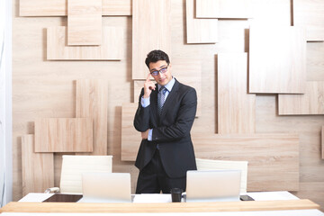 Handsome serious businessman in black suit standing at the desk and working on laptop in the modern office	