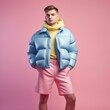 Beautiful man with glasses and brown hair posing in blue puff winter jacket on pastel pink backgroun. Generative AI.