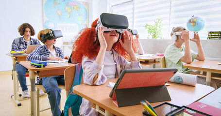 Interactive school concept. Kids in VR headsets sitting at desks and having virtual reality learning experience. Study technology. Kids in VR glasses in classroom. Tech education.