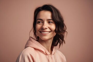 Wall Mural - Portrait of a beautiful young woman in pink hoodie smiling at camera isolated over beige background