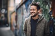 Environmental portrait photography of a grinning man in his 30s wearing a cozy sweater against a graffiti background. Generative AI