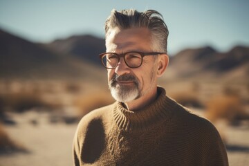 Poster - Handsome middle-aged man with gray hair and beard wearing brown sweater and eyeglasses in the desert