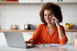 © Prostock-studio - Telecommuting Concept. Black Woman Working On Laptop And Using Cellphone In Kitchen