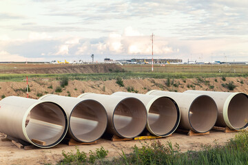 Stack of big frp composite fiberglass plastic sewage pipes at warehouse construction site near Leipzig Halle airport against blue sky background. Highway road construction infrastructure earthworks