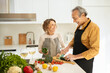 © Prostock-studio - Happy elderly spouses cooking together and talking, woman and man preparing vegetable salad, kitchen interior