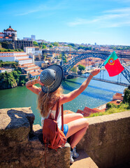 Wall Mural - Woman tourist holding portuguese flag enjoying beautiful view of Porto city and famous iron bridge- summer travel destination,  vacation, tourism in Portugal