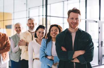 Cheerful businessman with crossed hands smiling at camera during daytime for collaborative brainstorming with involved employees in association synergy, happy Caucasian male boss enjoying teamwork