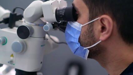 Wall Mural - Concentrated dentist with medical mask on face looking in innovative dental microscope checking cavity of patient at appointment high-quality equipment in dentistry clinic