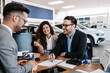 © Dusko - Middle age couple choosing and buying car at car showroom. Car salesman helps them to make right decision. Man signs buyers contract.