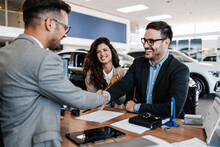 Middle Age Couple Choosing And Buying Car At Car Showroom. Car Salesman Helps Them To Make Right Decision. Man Signs Buyers Contract.