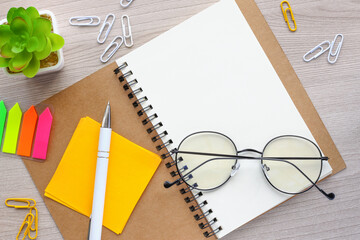 Wall Mural - top view image of an open notebook with blank pages next to a potted plant and colorful stickers on a wooden table. ready to add text or layout.